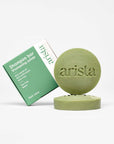 Green shampoo bar box beside a round green soap embossed with arista