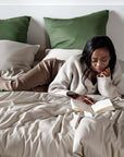 Woman reading a book on a bed with olive green and sand beige pillows.