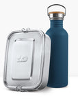 Navy blue non insulated bottle with a wooden lid and metal handle beside a metal lunch tin