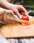 Hands slice a tomato with a bamboo knife on a wooden cutting board