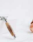 Close up of bamboo safety razor with wooden handle resting on a white marble surface