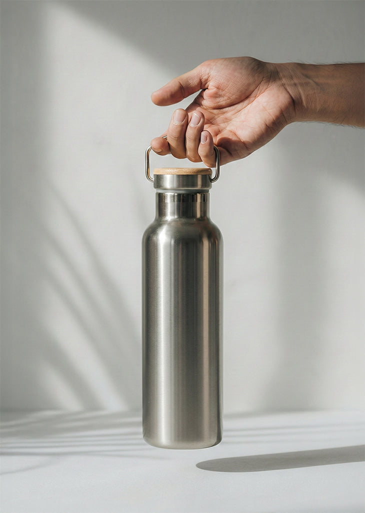 Hand holding a Bambaw silver stainless steel water bottle against a neutral background