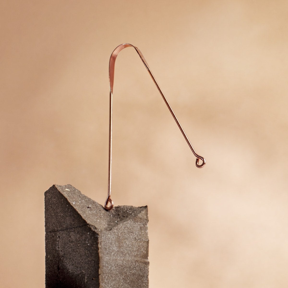 Copper tongue scraper with curved wire design balanced on a gray rock block