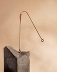Copper tongue scraper with curved wire design balanced on a gray rock block