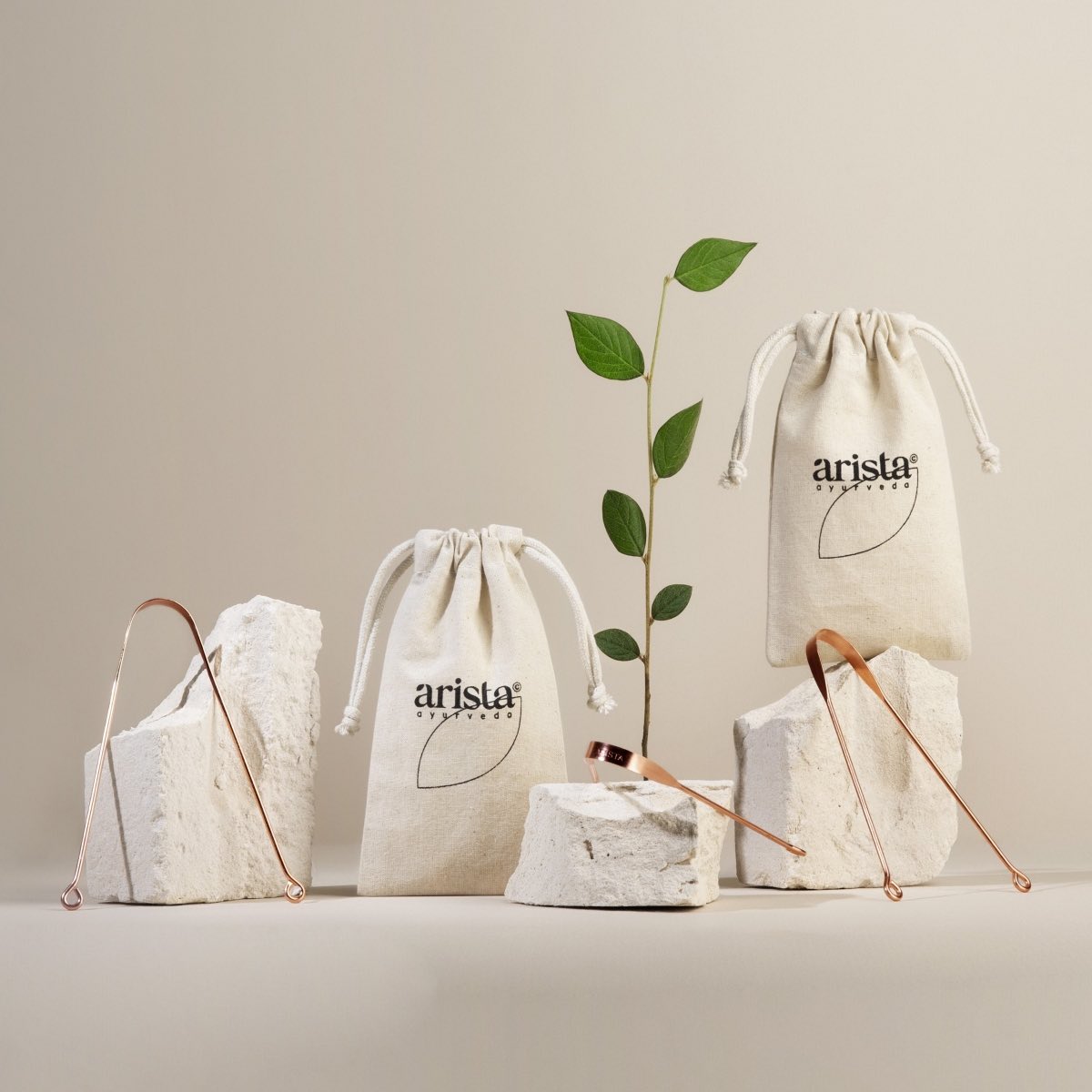 Two beige drawstring pouches with the arista logo displayed among rocks and copper tongue scrapers