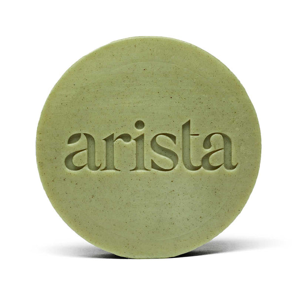 Close-up of pale green round arista shampoo bar with embossed lettering