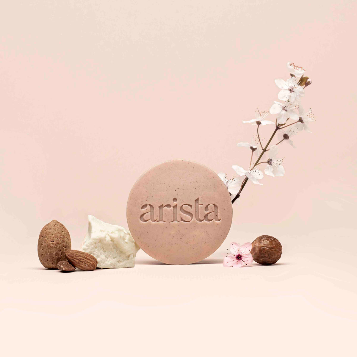 Round pale pink shampoo bar for curly hair embossed with arista logo beside blossoms