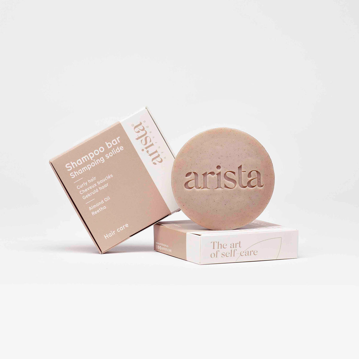 Shampoo bar packaging and a speckled round shampoo bar arranged together for curly hair care