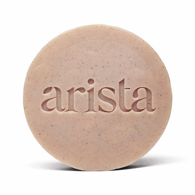 Close up of a round speckled shampoo bar for curly hair with the arista branding on its surface