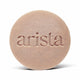 Close up of a round speckled shampoo bar for curly hair with the arista branding on its surface