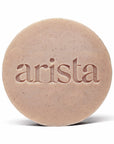 Close up of a round speckled shampoo bar for curly hair with the arista branding on its surface