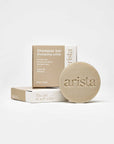 Beige shampoo bar packaging with arista branding and the round bar beside it.