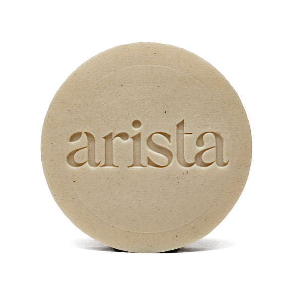 Beige round shampoo bar with arista embossed across the center.