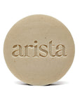 Beige round shampoo bar with arista embossed across the center.