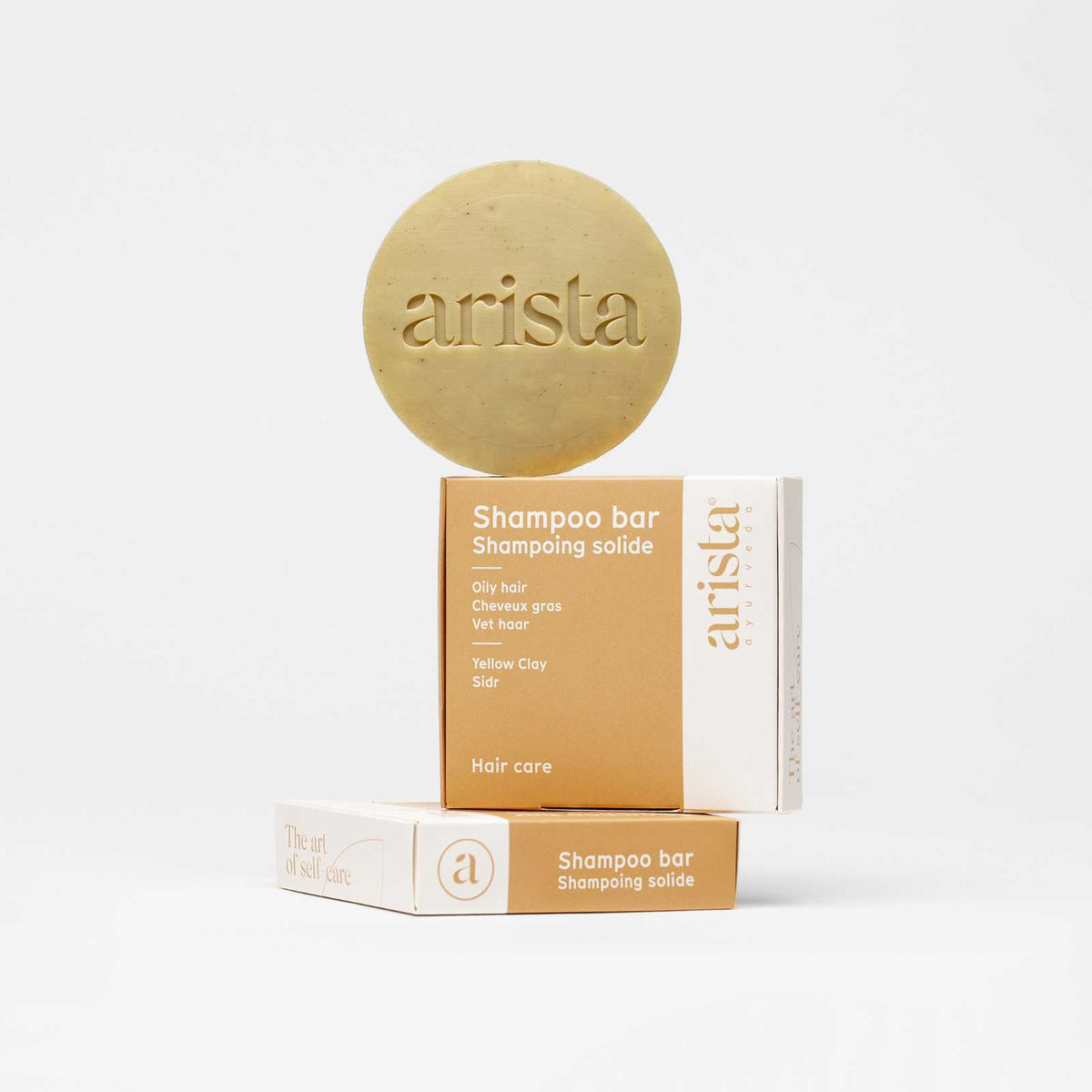 Beige circular shampoo bar for oily hair embossed with arista beside stacked hair care boxes