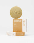 Beige circular shampoo bar for oily hair embossed with arista beside stacked hair care boxes