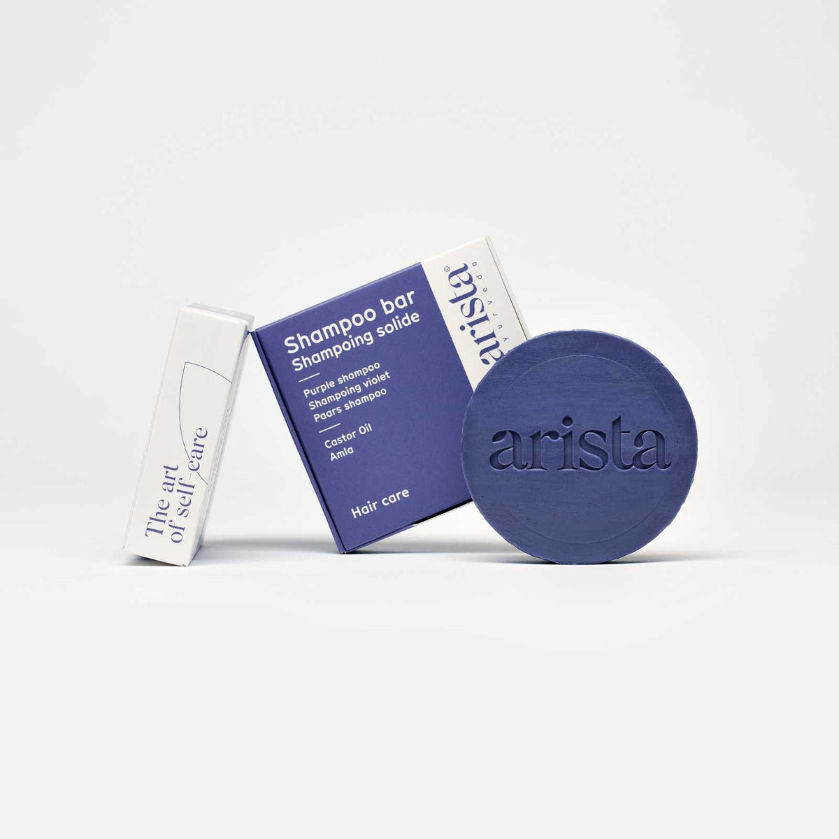 Purple circular shampoo bar with arista branding beside a blue box on a white surface