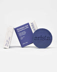 Purple circular shampoo bar with arista branding beside a blue box on a white surface