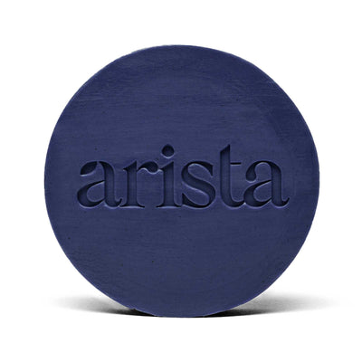 Deep blue circular shampoo bar with arista logo embossed on its surface