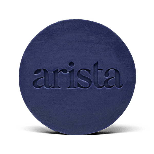 Deep blue circular shampoo bar with arista logo embossed on its surface