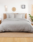 Bed dressed in a cool gray Bamboo Duvet Cover with gray pillows against a white wall and woven accents