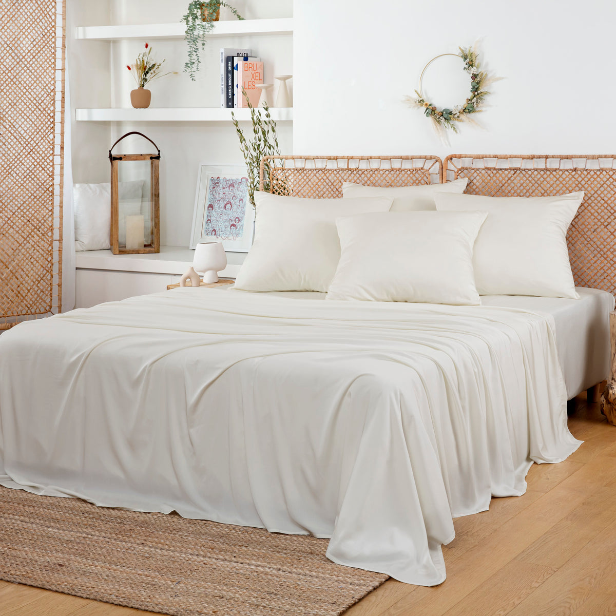 Bedroom with white bedding and a bamboo framed headboard, neutral rug and greenery accents