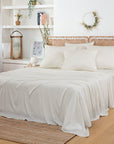 Bedroom with white bedding and a bamboo framed headboard, neutral rug and greenery accents