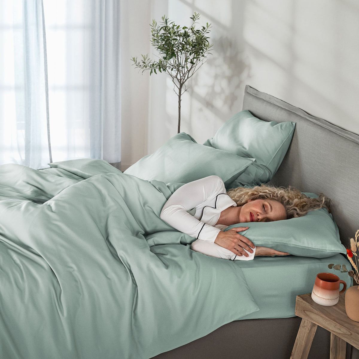 Woman lying in bed with light green bedding in a bright bedroom.