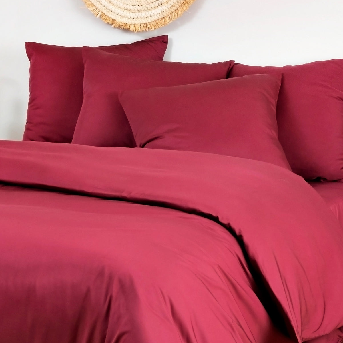 Two deep burgundy bamboo pillowcases on a bed against a white wall.