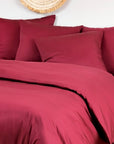 Two deep burgundy bamboo pillowcases on a bed against a white wall.