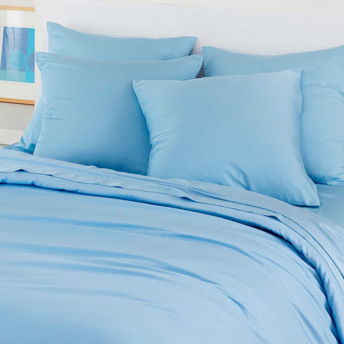 Light blue bamboo pillowcases pack of 2 arranged on a bed with a white headboard and framed print