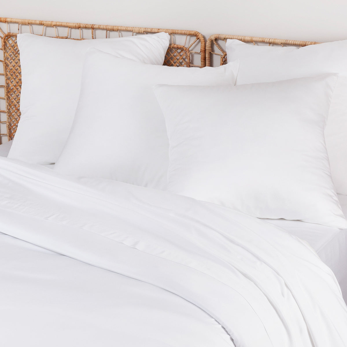 Side view of a bed with white pillows and a wicker headboard in a clean bedroom