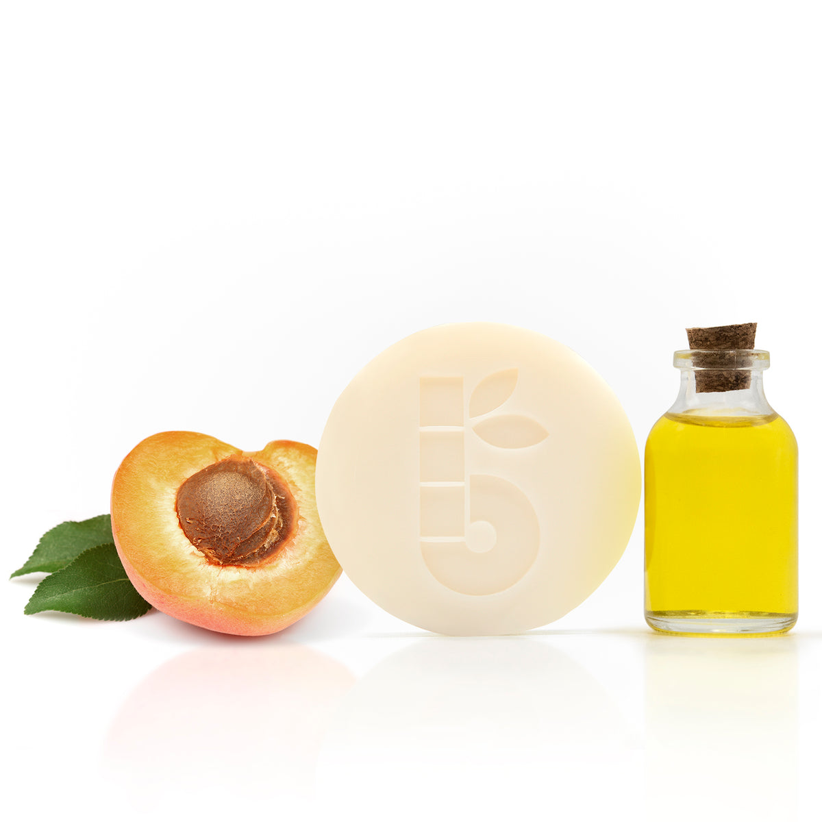 Round ivory shaving soap with a peach half and a bottle of oil on a white background