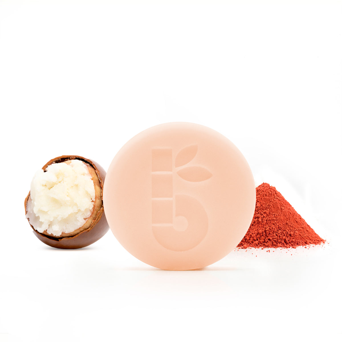 Peach round shaving bar with a leaf imprint beside a macaron half and a red powder pile