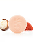 Peach round shaving bar with a leaf imprint beside a macaron half and a red powder pile