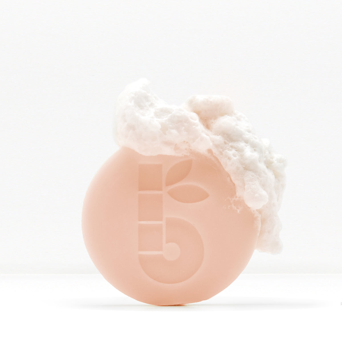 Shaving bar with foamy lather on top held in a hand against a white background