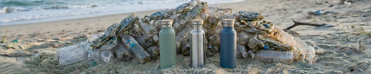 Three Bambaw insulated water bottles on a sandy beach with ocean and used plastic bottles in the background desktop banner strip