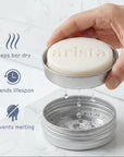 Hand holds round aluminium tin with white arista soap bar; icons indicate keeps bar dry extends lifespan prevents melting