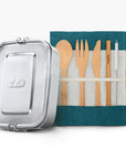 Metal lunch tin beside a teal roll up pouch with wooden spoon fork and knife for a back to school bundle