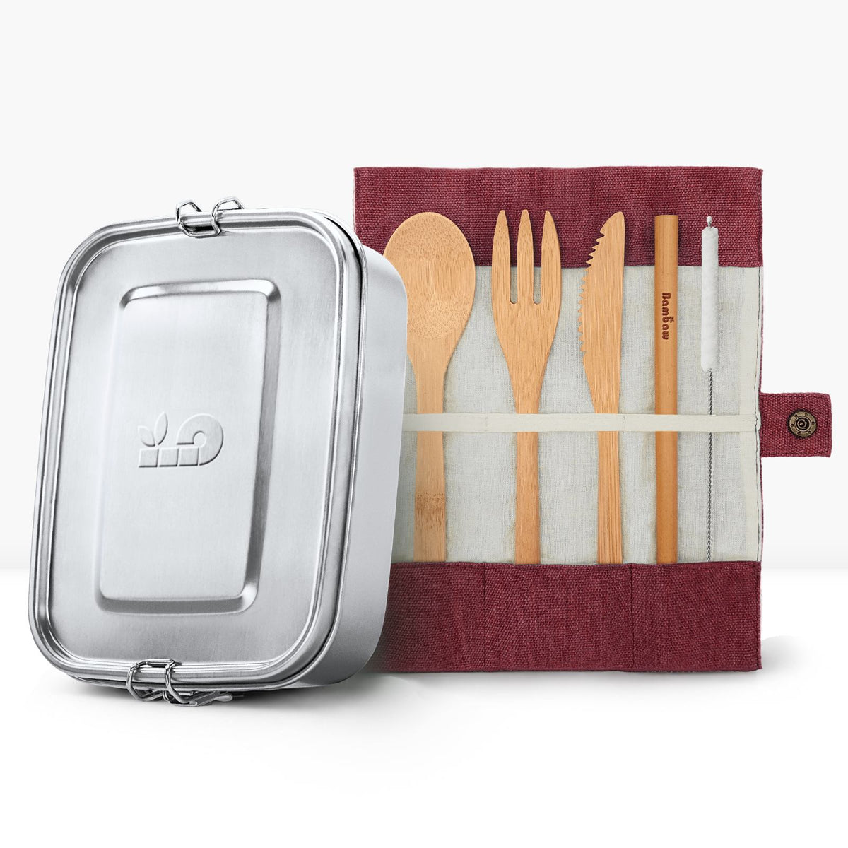 Silver lunch tin beside a red fabric utensil roll with wooden spoons and a serrated knife.