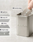 Metal razor blade holder with blades and a hand taking a blade, on a light gray background.