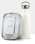Cream white non insulated bottle with a wooden lid and metal handle beside a metal lunch tin