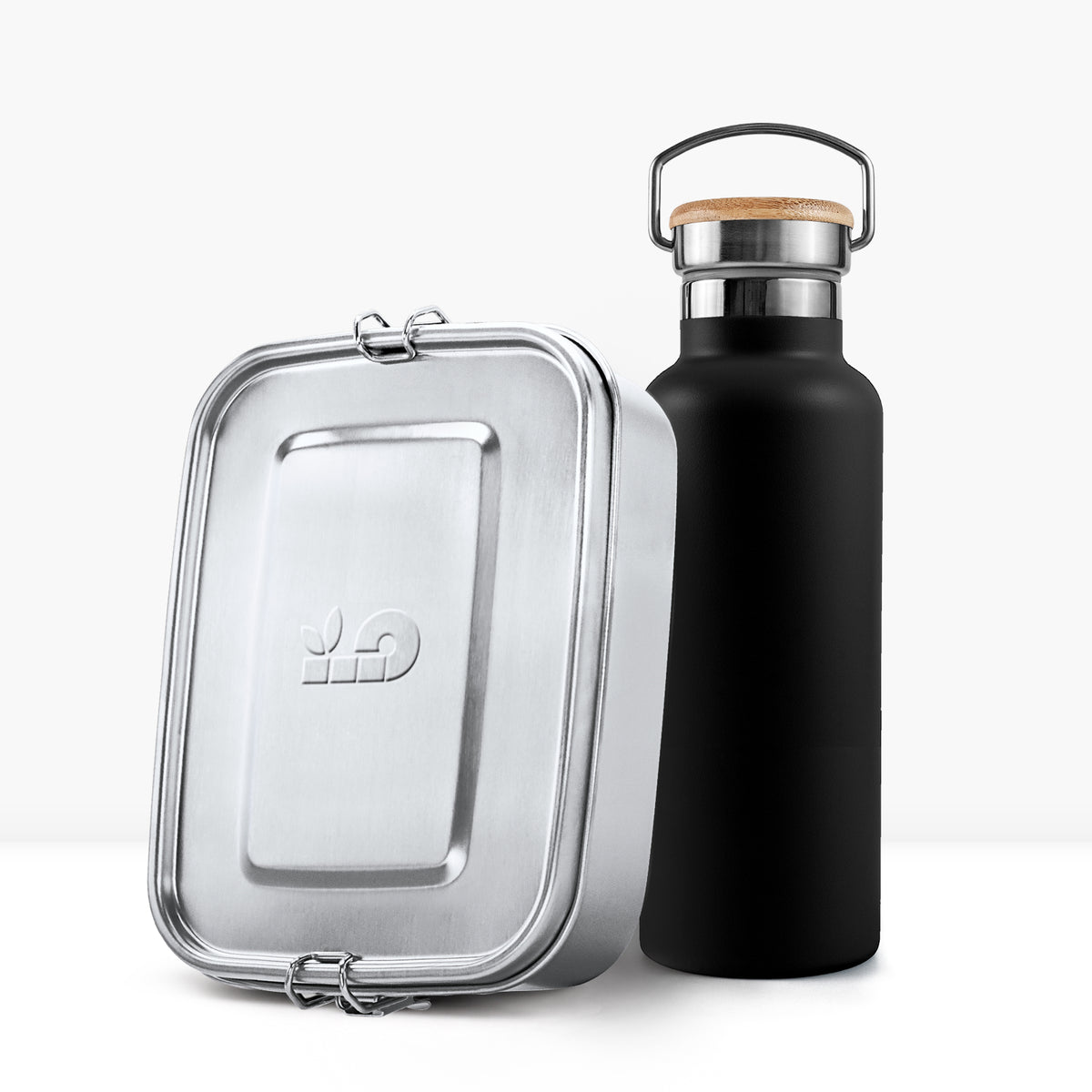 Close up of a silver metal lunch tin beside a matte black insulated bottle with a wooden cork lid