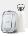 Silver metal lunch tin with hinged clasp beside a white insulated bottle topped with a cork lid and metal handle.