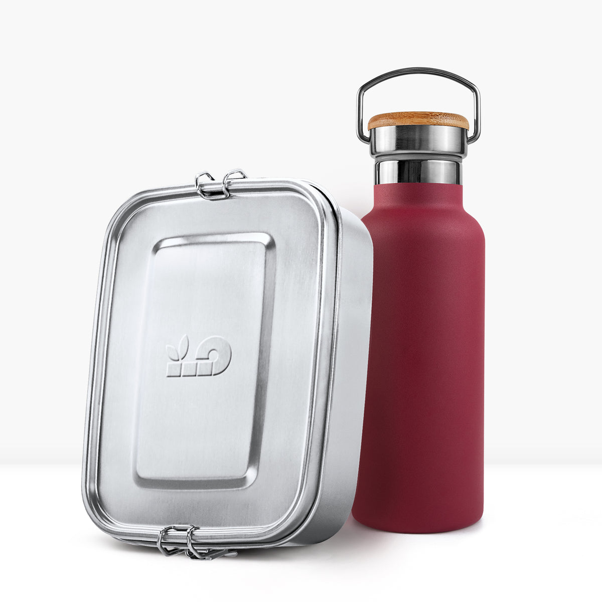Close up of a red insulated bottle with a cork lid next to a silver lunch tin