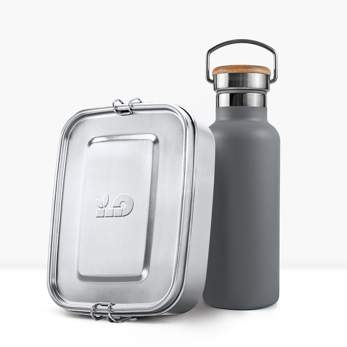 Grey insulated bottle with cork cap and metal handle beside a silver lunch tin.