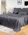 A bed dressed in charcoal bambaw cozy bamboo bedding bedding, including a sheet, duvet, and matching pillowcases, styled in a bright bedroom with a mirror, side table, framed wall art, and light wood floor.