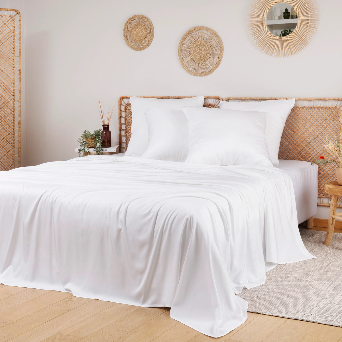 White bamboo bedding set on a bed with a wicker headboard in a room with decorative mirrors and plants.