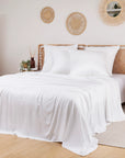 White bamboo bedding set on a bed with a wicker headboard in a room with decorative mirrors and plants.