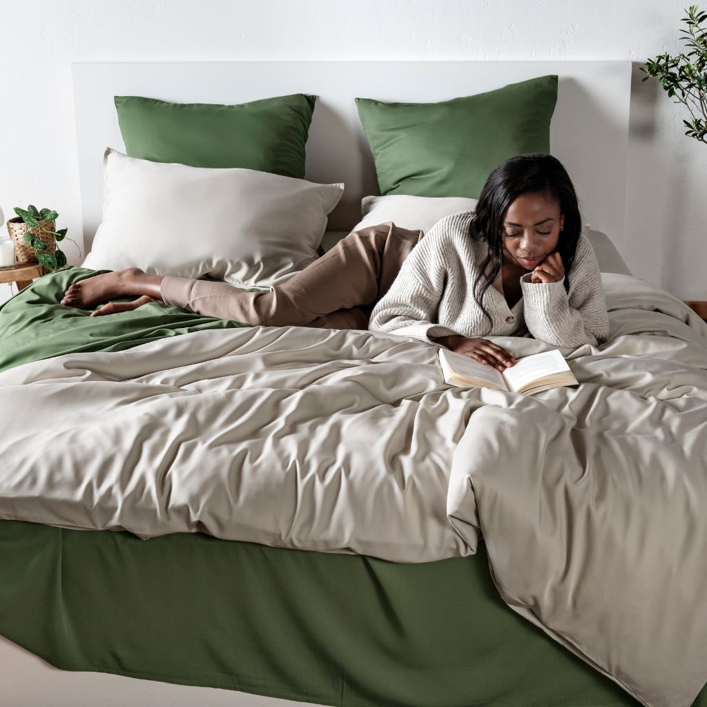 Woman reading a book on a bed with green and sand bamboo bedding